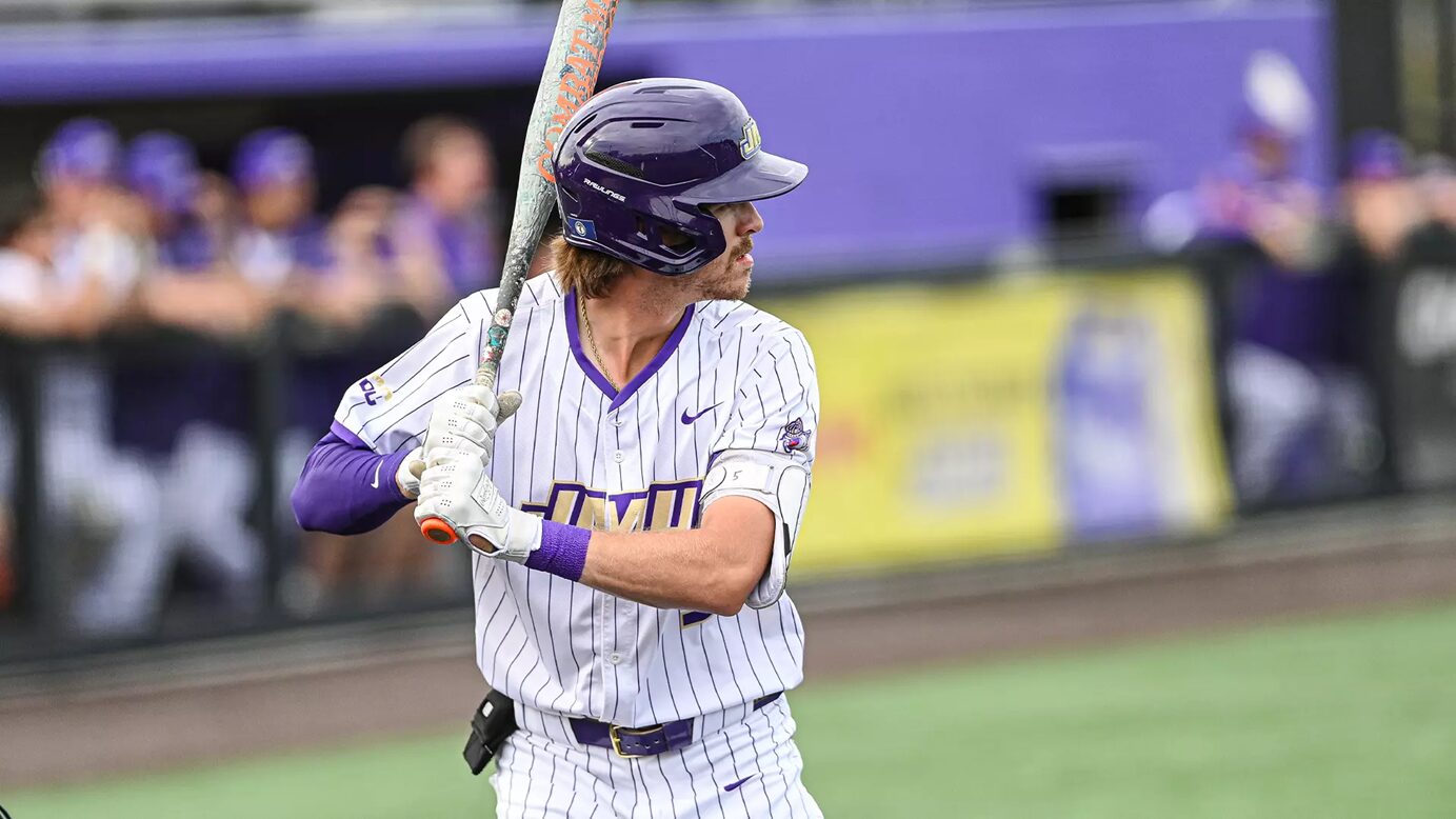 Baseball player in white pinstripe uniform with purple accents, helmet on, mid-swing with bat during a game.