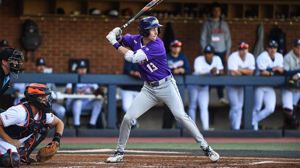 Baseball batter in purple jersey swinging at a pitch, with catcher behind home plate and umpire nearby