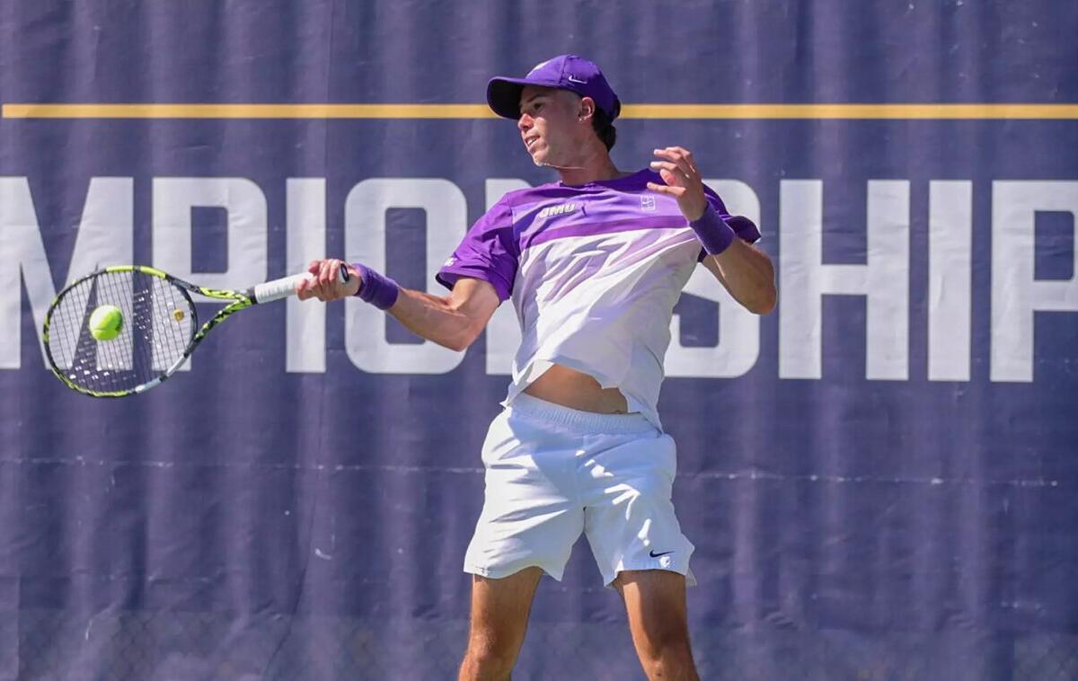 Tennis player in a purple cap and shirt hits a forehand during a championship match, ball near the racket on a blue court backdrop.