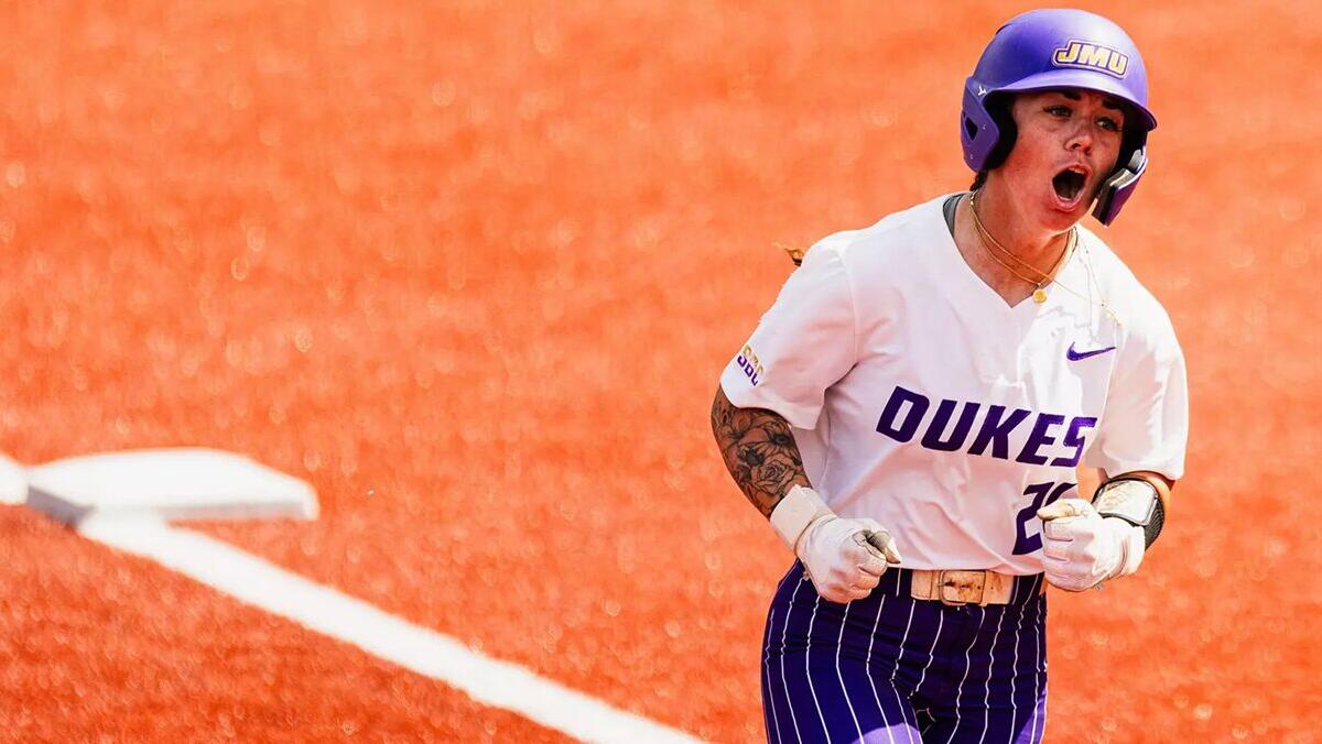 Dukes softball player sprinting on an orange infield, helmet on, fists clenched in celebration.