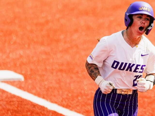 Dukes softball player sprinting on an orange infield, helmet on, fists clenched in celebration.