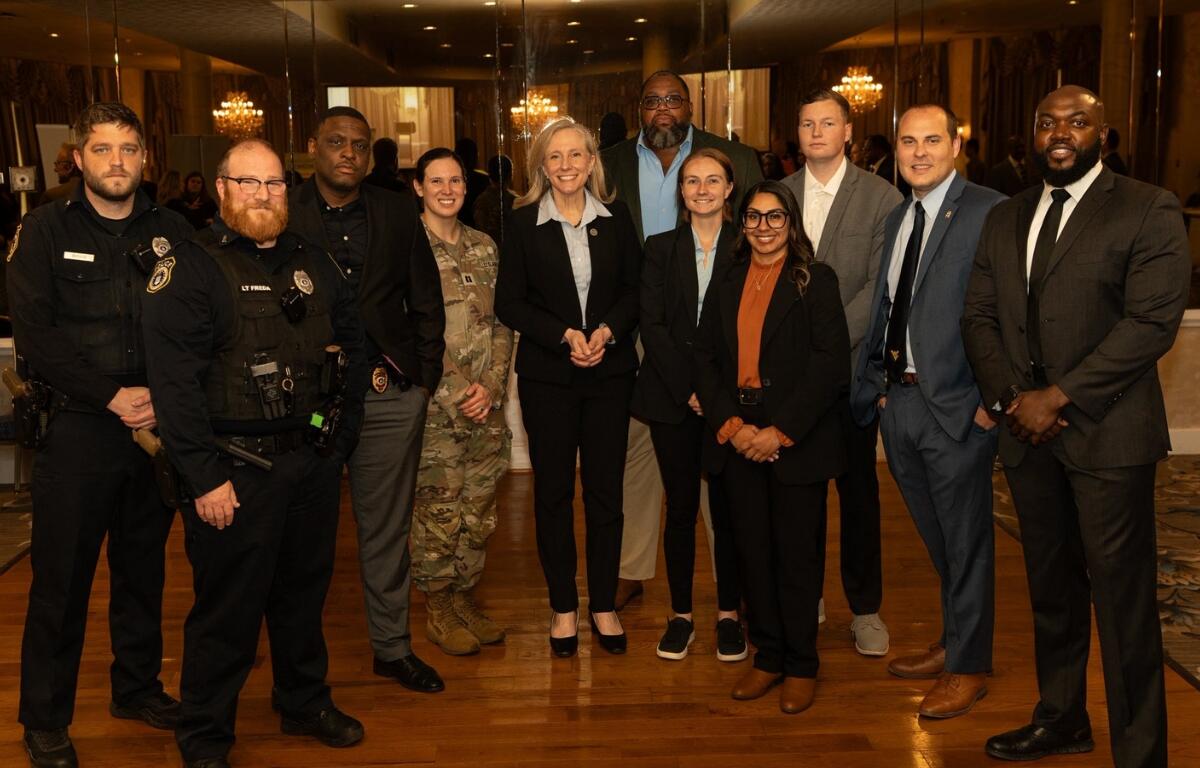 Group of ten professionals in business attire and security uniforms posing for a photo in a formal venue with chandeliers and mirrors in the background.