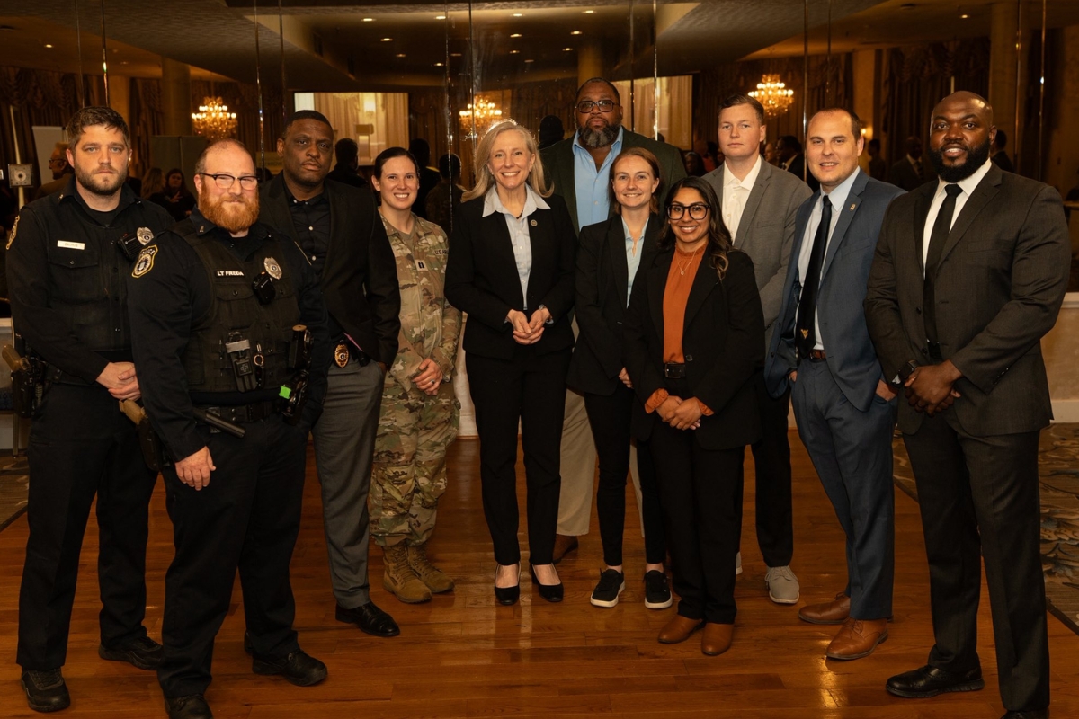 Group of ten professionals in business attire and security uniforms posing for a photo in a formal venue with chandeliers and mirrors in the background.