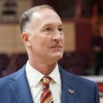 Professional portrait of a middle-aged man in a blue suit and striped tie, wearing a VT pin, looking to the right in an indoor venue.