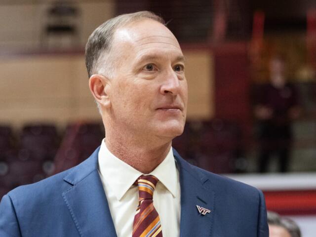 Professional portrait of a middle-aged man in a blue suit and striped tie, wearing a VT pin, looking to the right in an indoor venue.