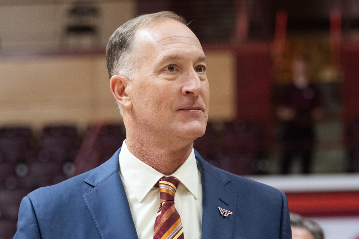 Professional portrait of a middle-aged man in a blue suit and striped tie, wearing a VT pin, looking to the right in an indoor venue.