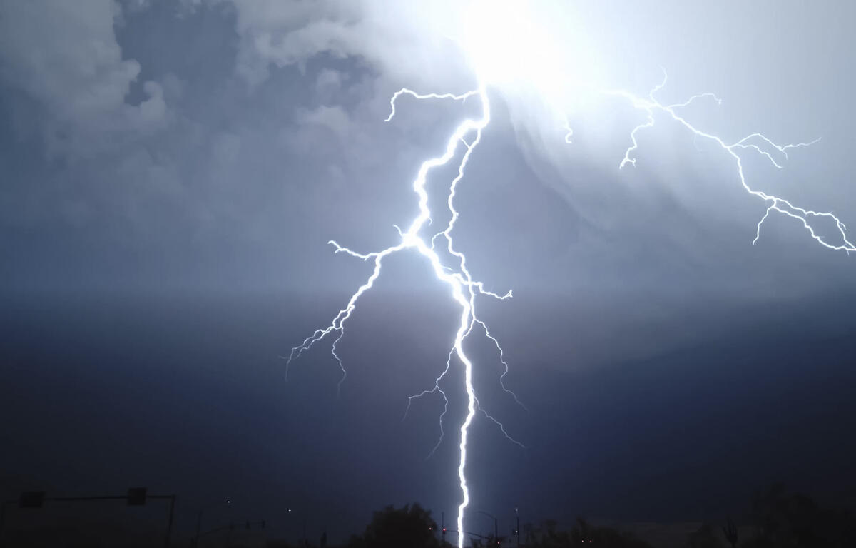 Bright lightning bolts strike downward over a dark, stormy sky above a silhouetted landscape at dusk/dark.