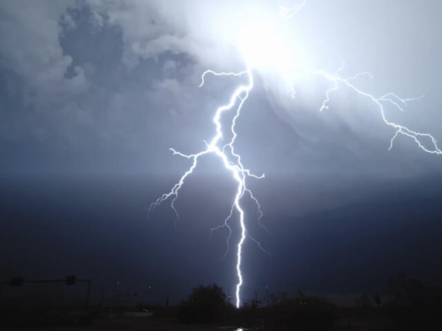 Bright lightning bolts strike downward over a dark, stormy sky above a silhouetted landscape at dusk/dark.
