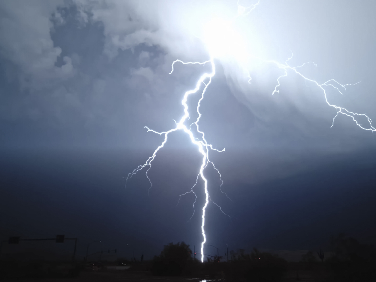 Bright lightning bolts strike downward over a dark, stormy sky above a silhouetted landscape at dusk/dark.
