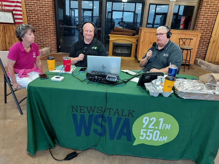 Three radio hosts broadcast live at a WSVA News Talk table with microphones, headphones, and a laptop in a brick studio setting