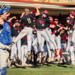 Bridgewater College Eagles baseball team celebrating on the field, players in black jerseys jumping with arms raised after a win.