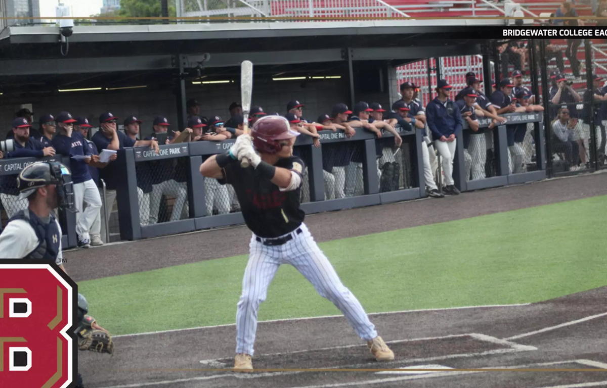 Baseball batter in black swings at home plate as teammates watch from the dugout; Bridgewater College Eagles insignia bottom-left.