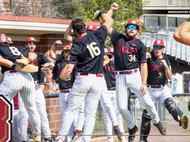 Bridgewater College Eagles baseball team celebrating a win with high-fives at the dugout, players in black jerseys and white pinstriped pants.