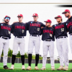 Bridgewater College Eagles baseball team stands in a line with arms around each other on the field, wearing black jerseys and pinstripe pants.