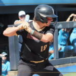 Baseball player in black uniform swinging a bat during a game, Bridgewater College Eagles on the jersey, crowd in the background.