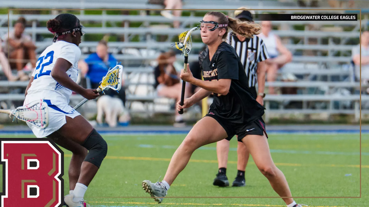 Lacrosse players in black and white uniforms compete for the ball on a turf field during a game, with a Bridgewater College Eagles logo visible in the corner.