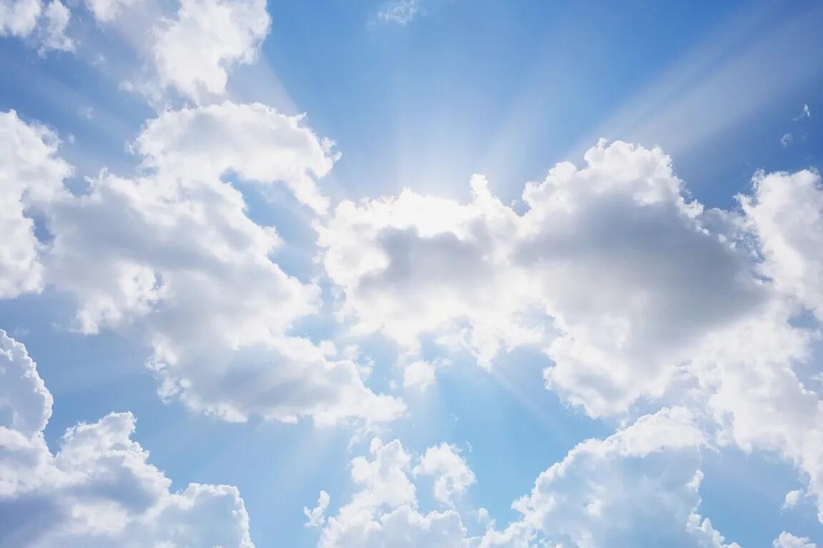 Bright blue sky with scattered white clouds and sunbeams radiating from behind them (sunlight breaking through the clouds).