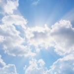 Bright blue sky with scattered white clouds and sunbeams radiating from behind them (sunlight breaking through the clouds).
