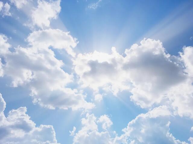 Bright blue sky with scattered white clouds and sunbeams radiating from behind them (sunlight breaking through the clouds).