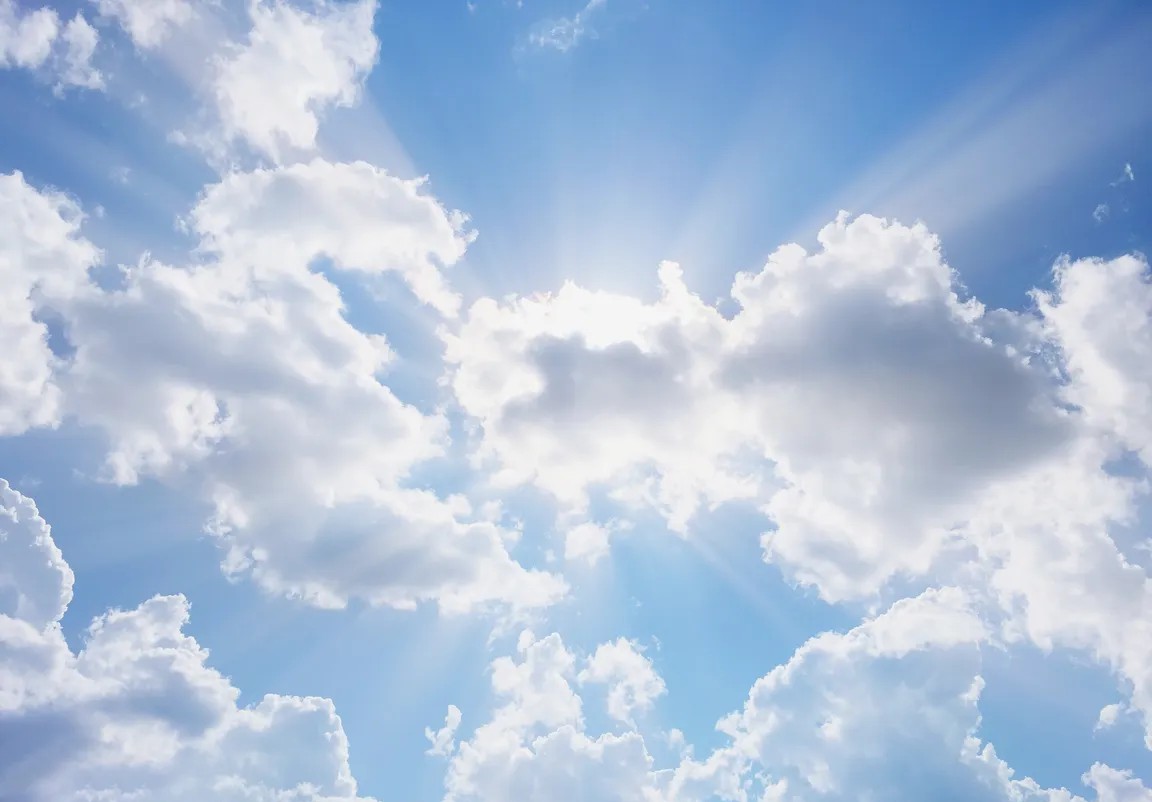 Bright blue sky with scattered white clouds and sunbeams radiating from behind them (sunlight breaking through the clouds).