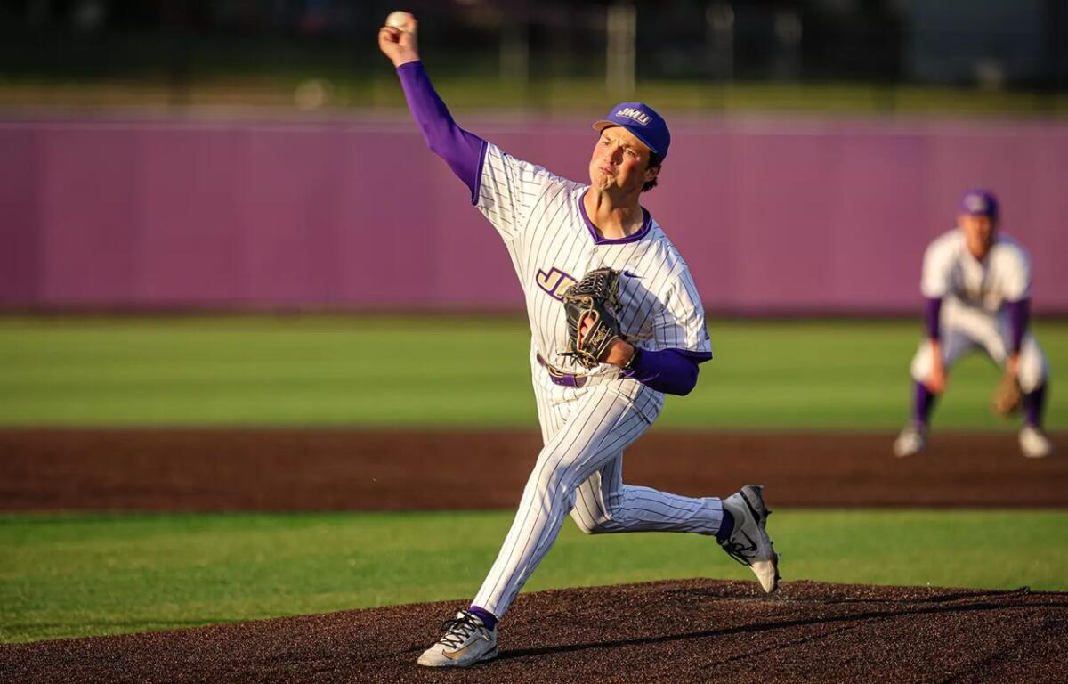 Baseball pitcher in a pinstriped uniform delivering a throw on the mound, purple accents, purple cap, with a fielder in the background