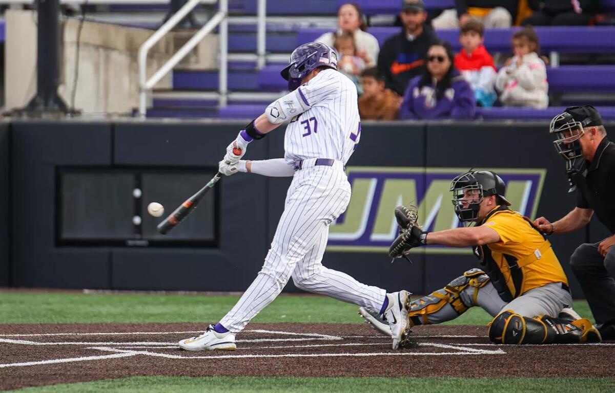 Baseball batter in white pinstripe uniform (-number 37) swings at a pitch as the catcher in yellow crouches behind home plate with an umpire nearby.