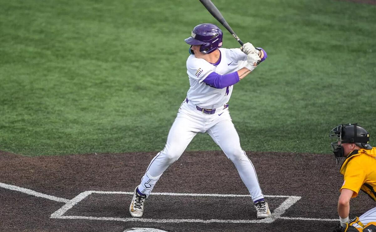 Baseball batter in white uniform swinging at a pitch, catcher in yellow crouched behind home plate.