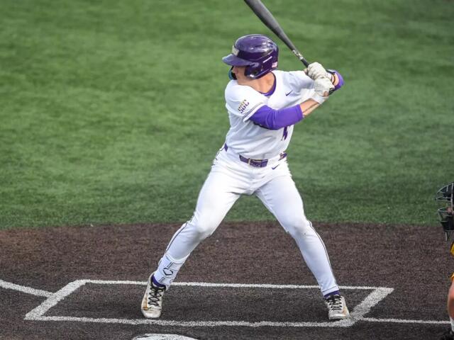 Baseball batter in white uniform swinging at a pitch, catcher in yellow crouched behind home plate.