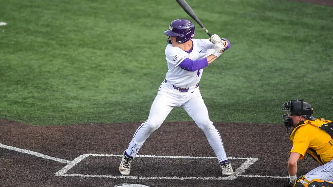 Baseball batter in white uniform swinging at a pitch, catcher in yellow crouched behind home plate.