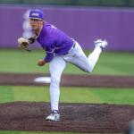 College baseball pitcher in purple uniform throwing from the mound, ball in midair behind him.
