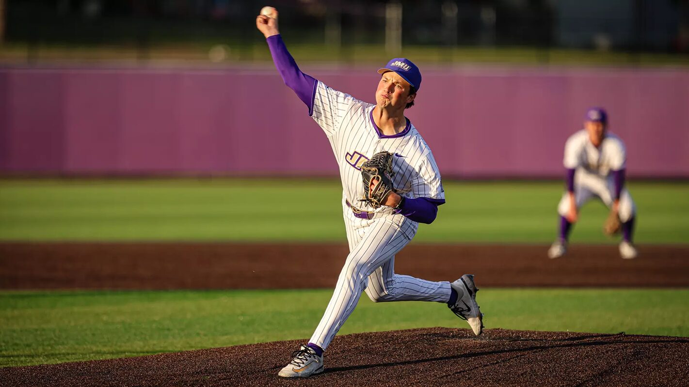 Baseball pitcher in a pinstriped uniform delivering a throw on the mound, purple accents, purple cap, with a fielder in the background