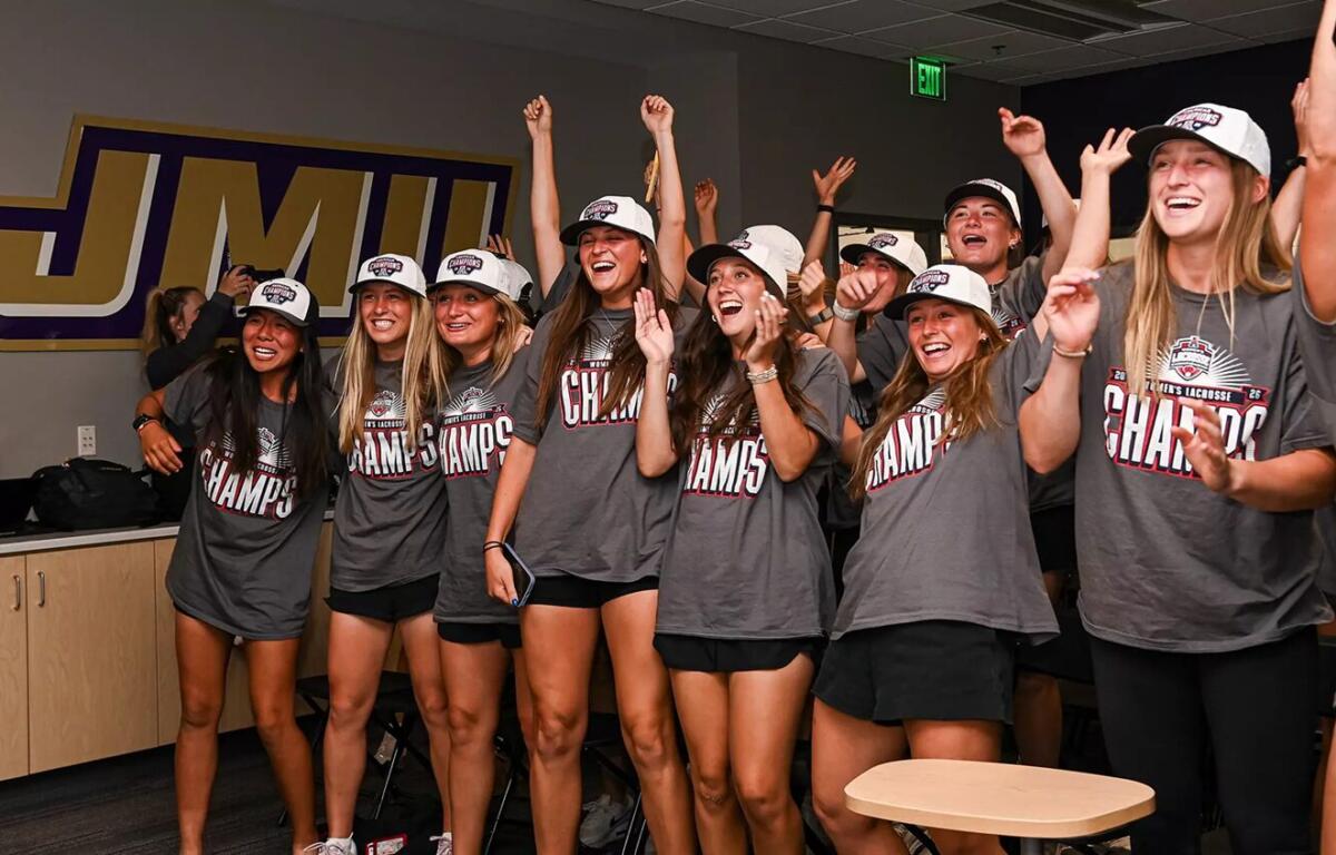 Group of young women in gray Champs shirts celebrate together in a locker-room, arms raised and smiling after a win.