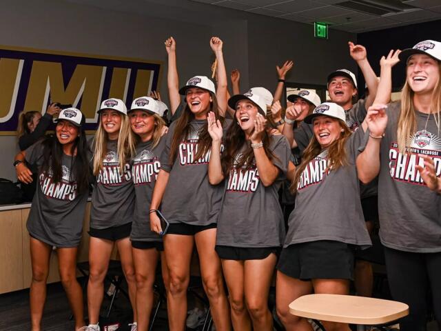 Group of young women in gray Champs shirts celebrate together in a locker-room, arms raised and smiling after a win.