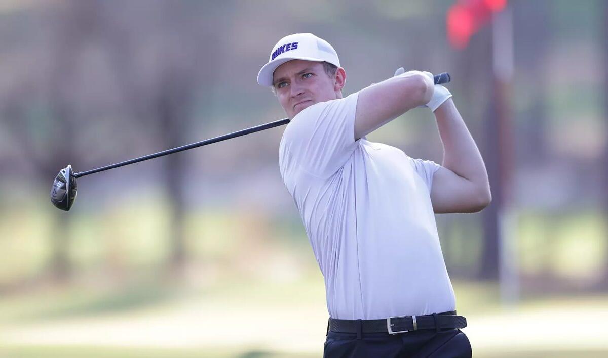 Male golfer in a white polo and cap mid-swing on a sunny golf course, focusing on his follow-through.
