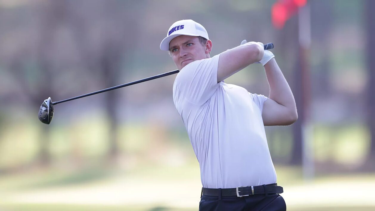 Male golfer in a white polo and cap mid-swing on a sunny golf course, focusing on his follow-through.