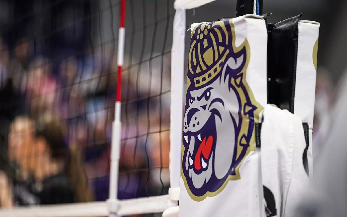 Close-up of a white padded goalpost with a bulldog mascot logo, with a blurred crowd in the background.