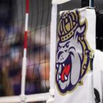 Close-up of a white padded goalpost with a bulldog mascot logo, with a blurred crowd in the background.