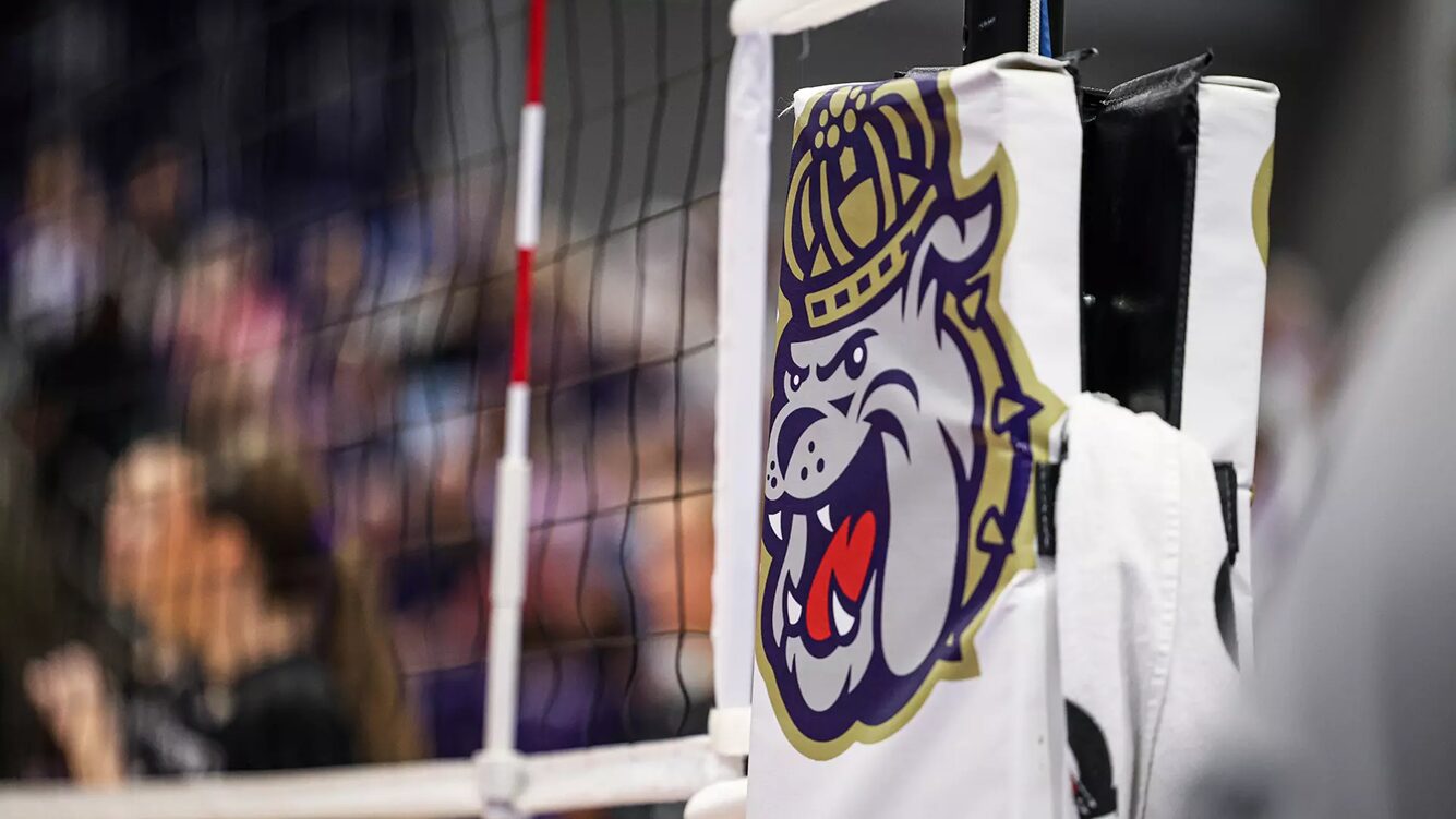 Close-up of a white padded goalpost with a bulldog mascot logo, with a blurred crowd in the background.