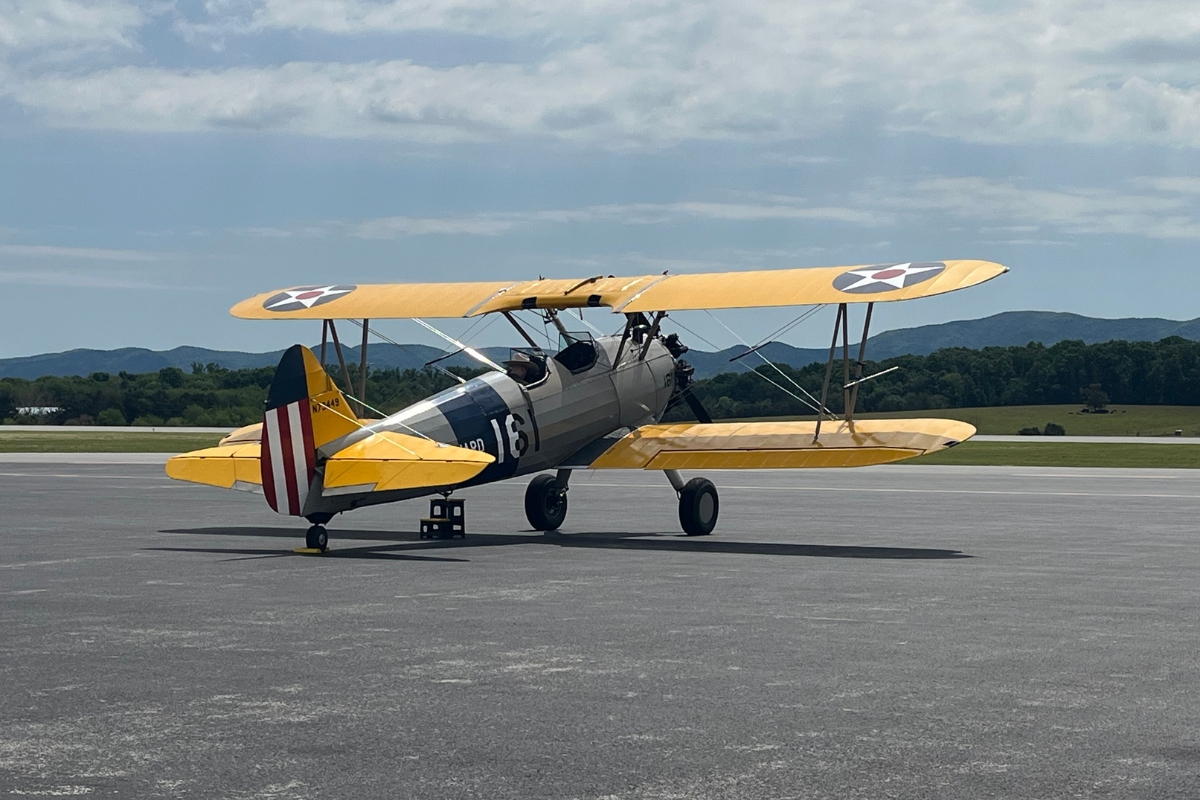 Yellow World War I–era biplane taxiing on a runway, silver fuselage with U.S. roundel insignia and a striped red‑white tail.