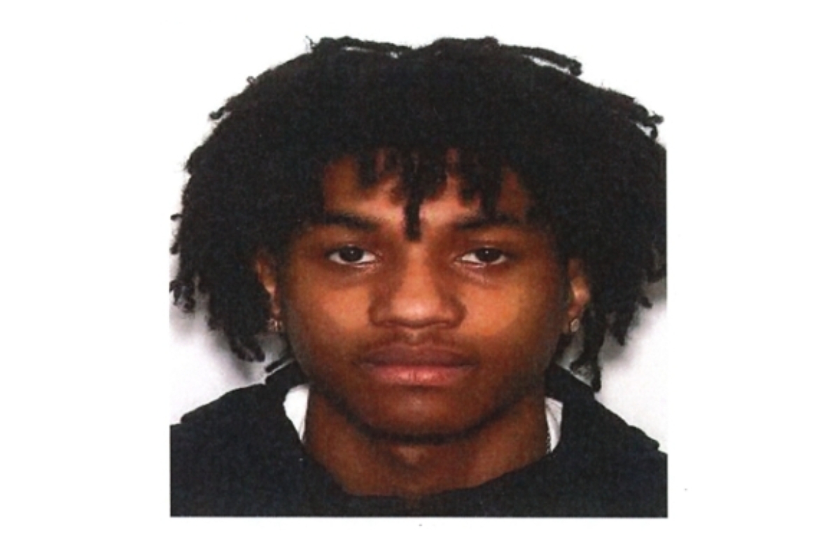 Head-and-shoulders portrait of a young man with dark dreadlocks, wearing a black top, neutral expression against a white background.