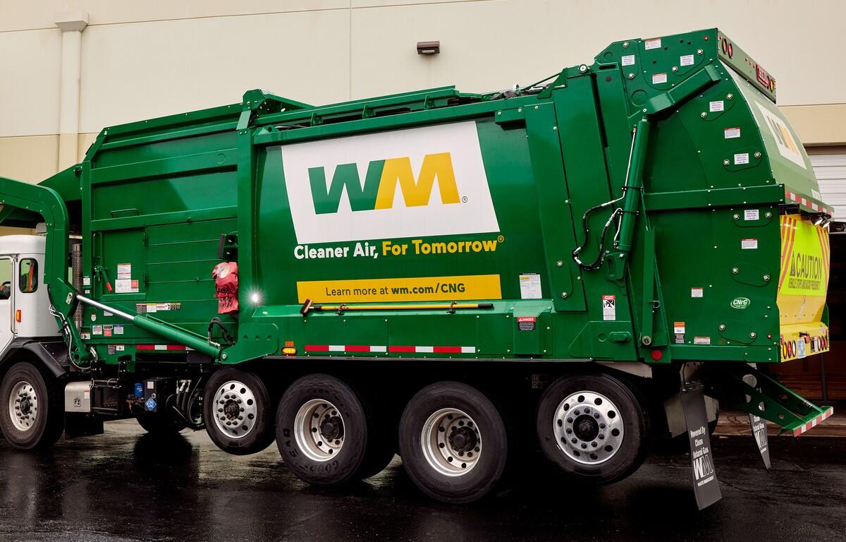 Green WM refuse truck with 'Cleaner Air, For Tomorrow' branding parked beside a building, showing large wheels and rear loading area.