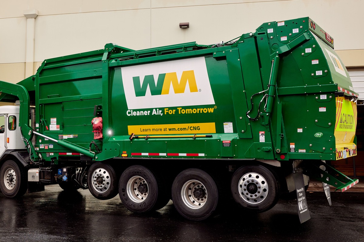 Green WM refuse truck with 'Cleaner Air, For Tomorrow' branding parked beside a building, showing large wheels and rear loading area.
