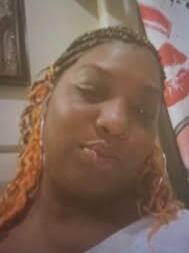 Close-up selfie of a person with orange braided hair puckering their lips in a bedroom setting with a leopard-pattern curtain in the background.