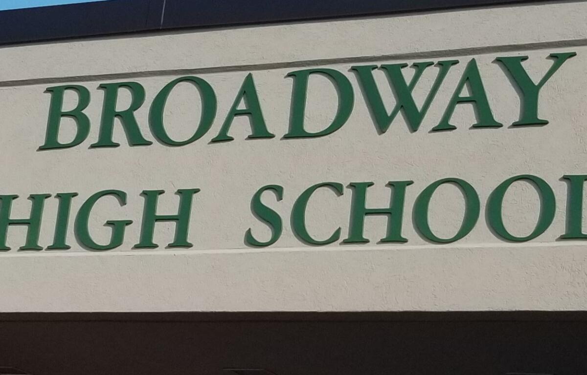 Exterior sign reading 'Broadway High School' in green letters on a beige wall.