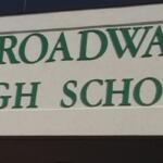Exterior sign reading 'Broadway High School' in green letters on a beige wall.