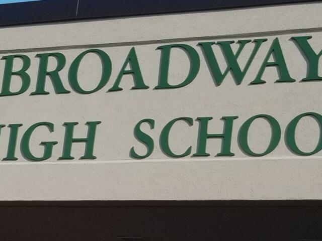 Exterior sign reading 'Broadway High School' in green letters on a beige wall.