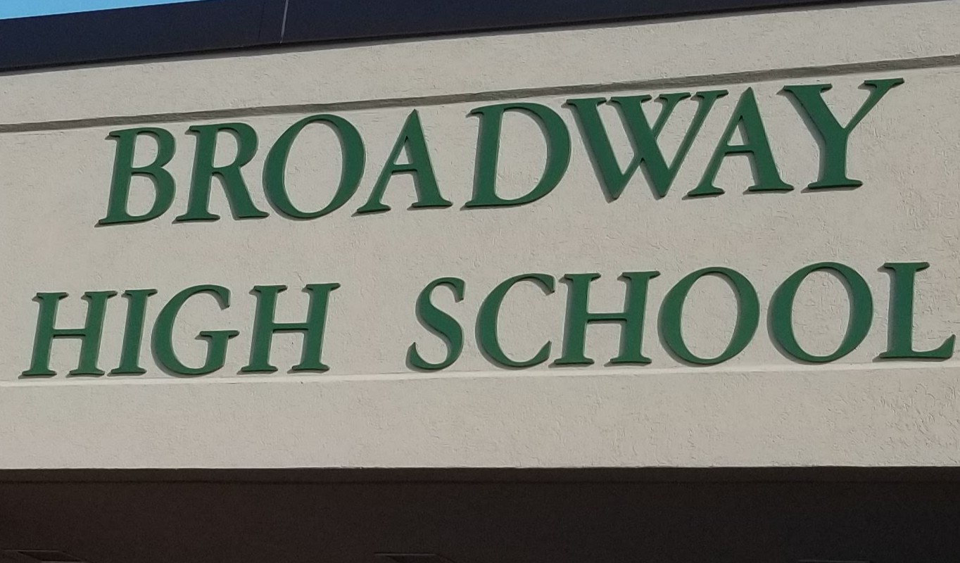 Exterior sign reading 'Broadway High School' in green letters on a beige wall.