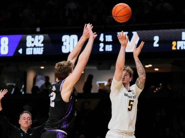 White jersey player #5 shoots the ball over a purple-jersey defender as the ball arcs upward.