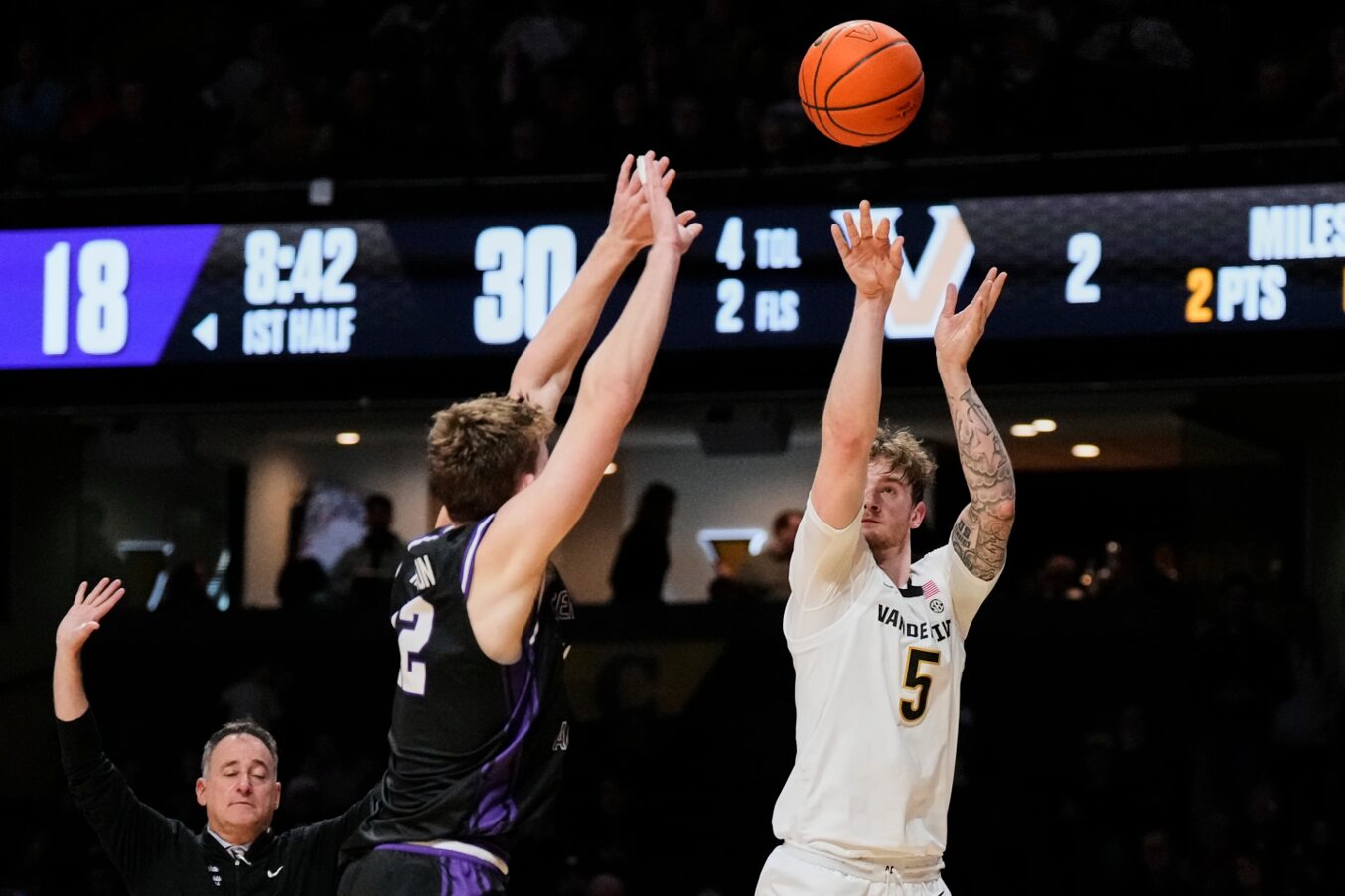 White jersey player #5 shoots the ball over a purple-jersey defender as the ball arcs upward.