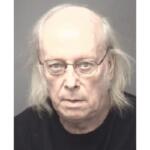 Mugshot of an older man with thin glasses, balding head and shoulder‑length gray hair, wearing a black shirt.